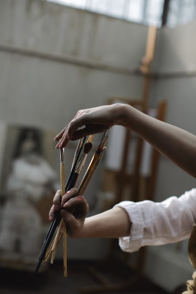 creativité Close-up of an artists hands holding paintbrushes indoors, showcasing creativity and artistry.