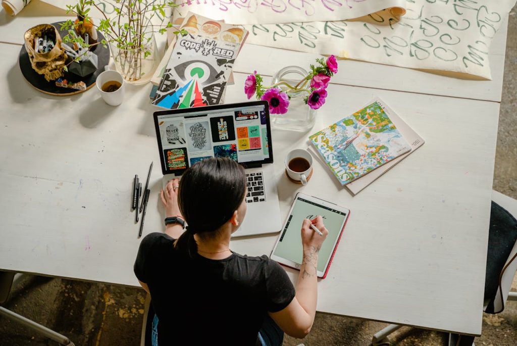 photo-of-woman-writing-on-tablet-computer-while-using-laptop-4348401 Artistic workspace featuring calligraphy and digital design on a tablet and laptop.