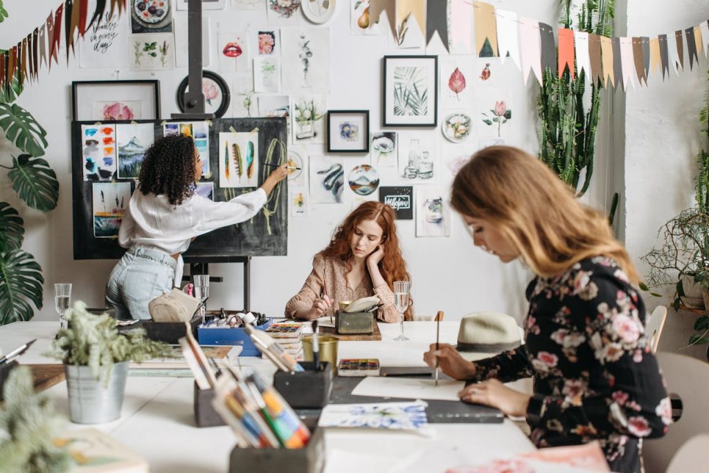 women-using-paintbrush-while-making-an-artwork-6925340 A lively art workshop with women painting and drawing creatively in an indoor setting.